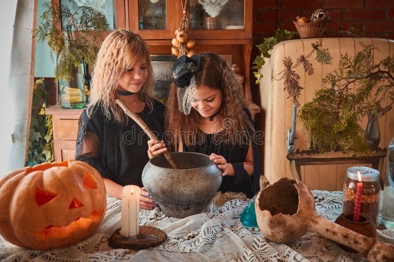 Two cute girls aged 10 years in witch costumes in an old house on Halloween brew a magic potion and conjure.