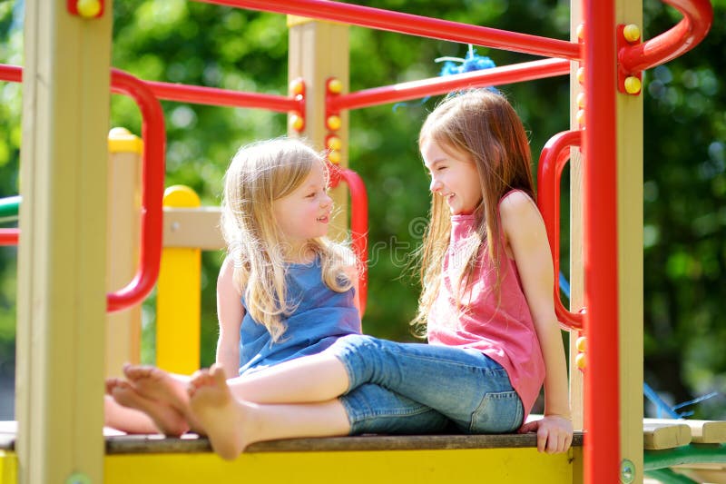 Two cute little girls having fun on a playground outdoors. 