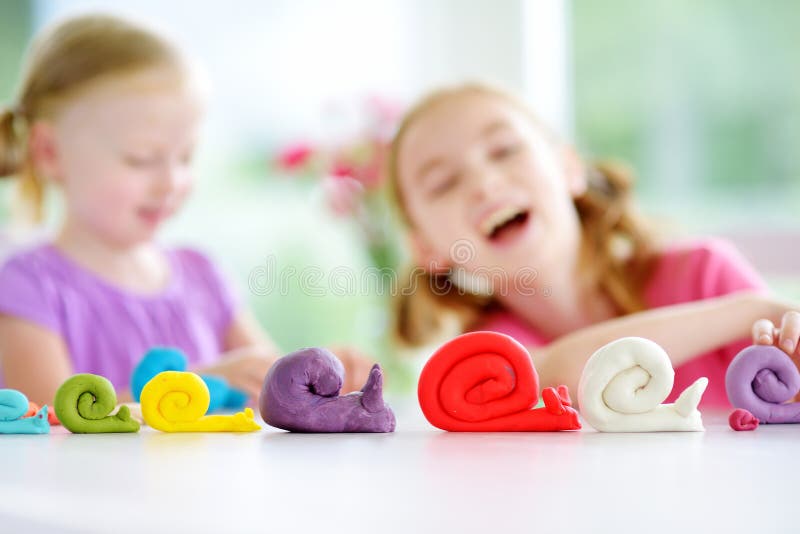 Two cute little sisters having fun together with modeling clay at a daycare. Creative kids molding at home. Children play with pla