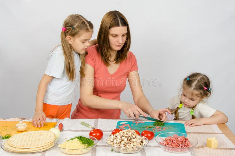 Two daughters are watching with interest as mother chopped green stock photos Two daughters are watching with interest as mother chopped green stock photos