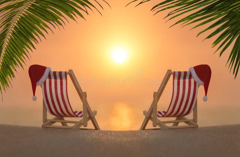 Two deckchairs with red Christmas Santa hats at ocean sandy palm sunset beach