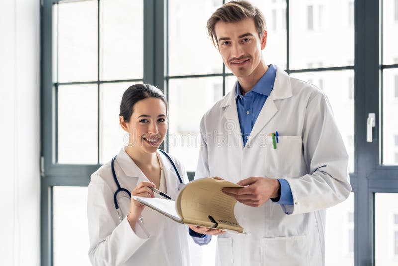 Two dedicated doctors smiling while holding a folder with medical records stock photos Two dedicated doctors smiling while holding a folder with medical records stock photos