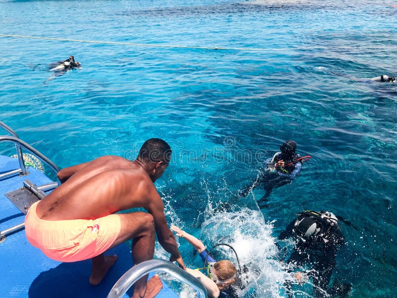 Two divers in black scuba diving suits, a man and a woman with oxygen bottles sink under the transparent blue water in the sea, th