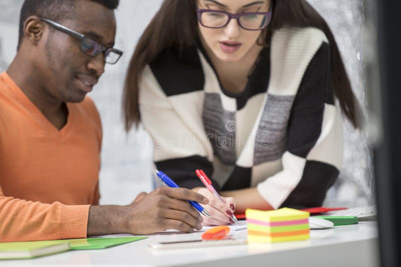 Two diverse work colleagues smiling and writing down notes while sitting together at a table in a modern office royalty free stock photography