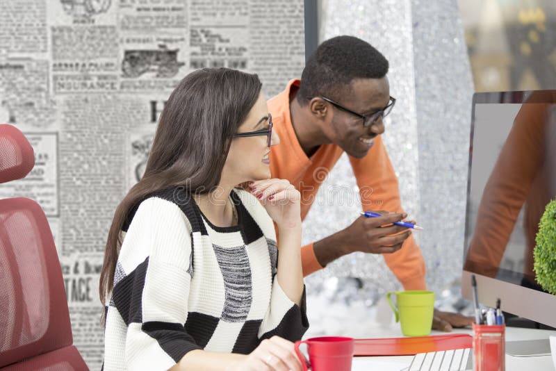 Two diverse work colleagues smiling and writing down notes while sitting together at a table in a modern office stock photo