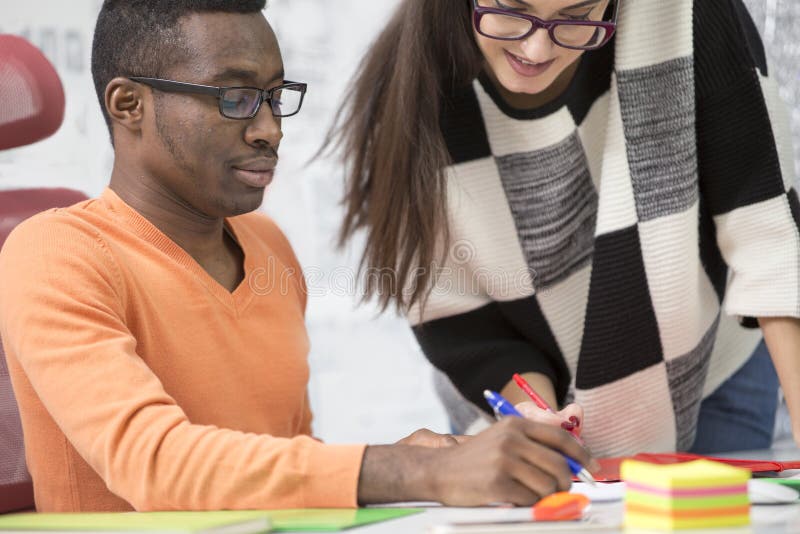Two diverse work colleagues smiling and writing down notes while sitting together at a table in a modern office royalty free stock images