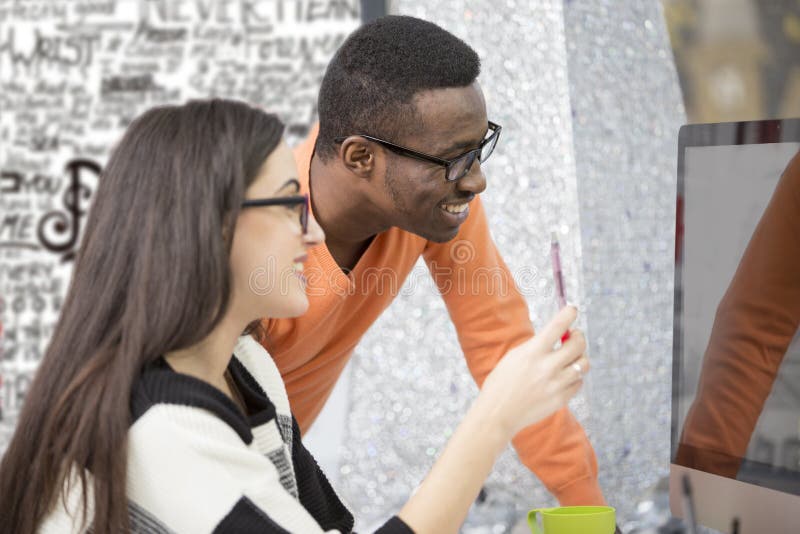 Two diverse work colleagues smiling and writing down notes while sitting together at a table in a modern office royalty free stock photography
