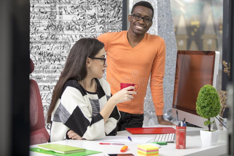 Two diverse work colleagues smiling and writing down notes while sitting together at a table in a modern office royalty free stock photos