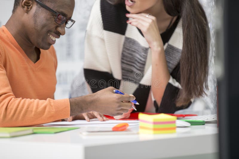 Two diverse work colleagues smiling and writing down notes while sitting together at a table in a modern office stock images
