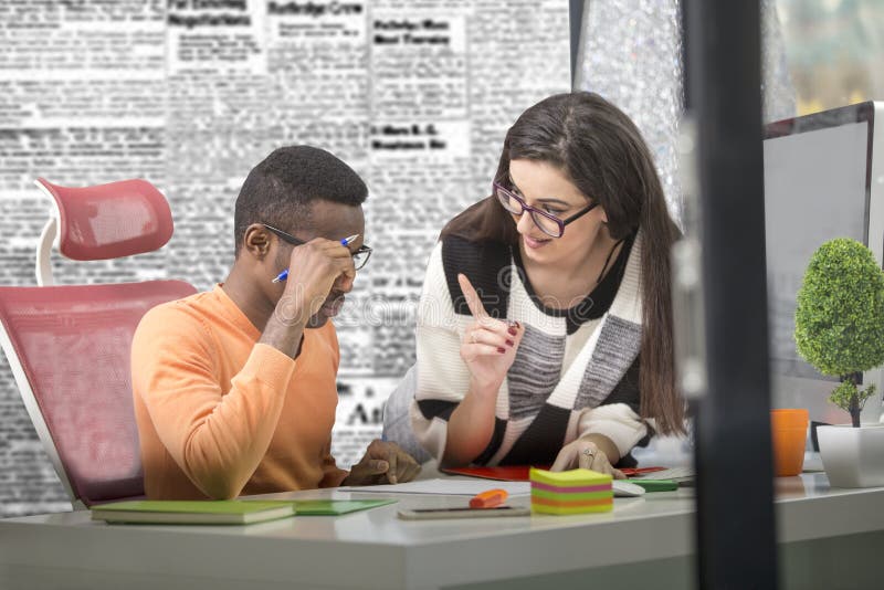 Two diverse work colleagues smiling and writing down notes while sitting together at a table in a modern office royalty free stock photography