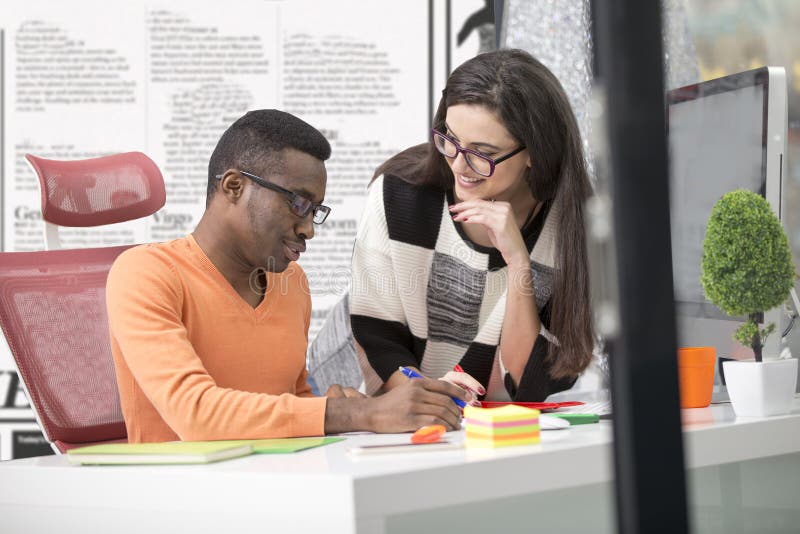 Two diverse work colleagues smiling and writing down notes while sitting together at a table in a modern office stock photography