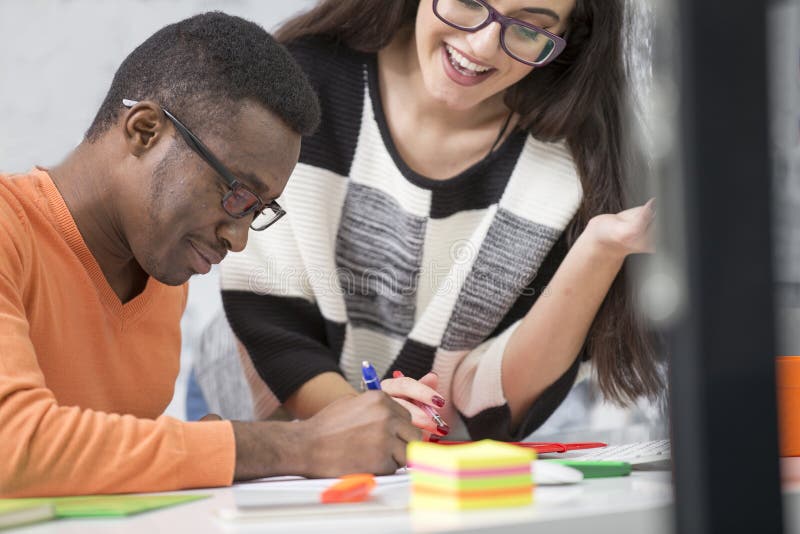 Two diverse work colleagues smiling and writing down notes while sitting together at a table in a modern office royalty free stock photos