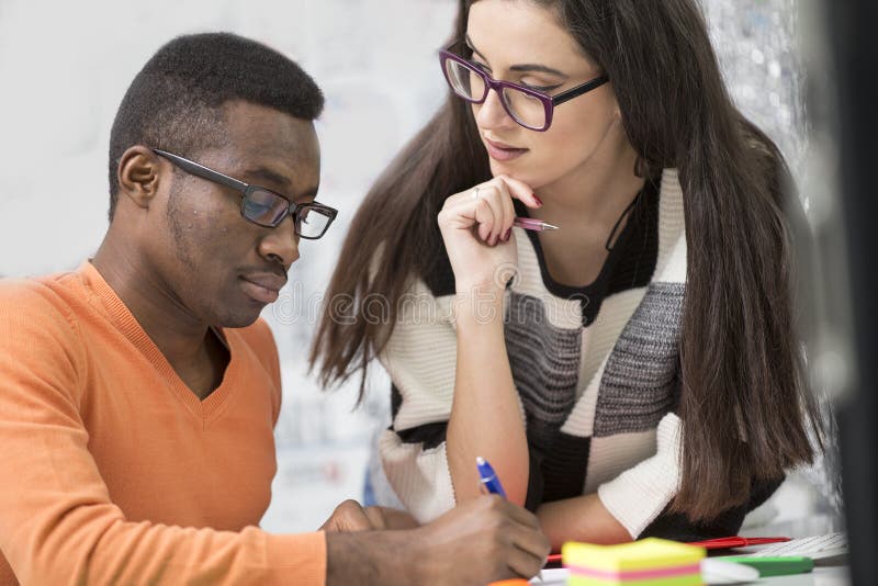 Two diverse work colleagues smiling and writing down notes while sitting together at a table in a modern office stock photography