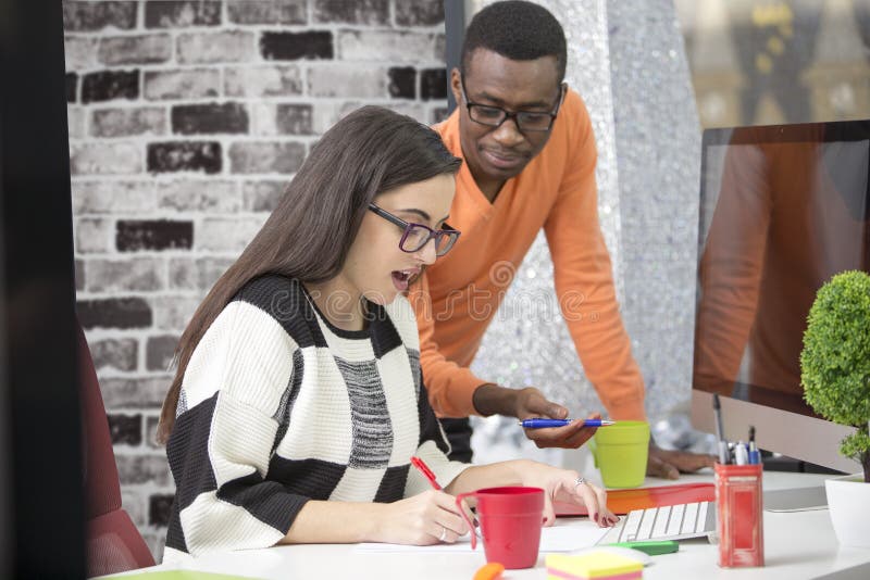 Two diverse work colleagues smiling and writing down notes while sitting together at a table in a modern office stock images