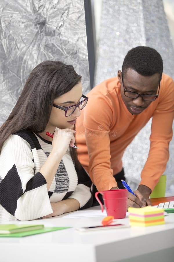 Two diverse work colleagues smiling and writing down notes while sitting together at a table in a modern office stock photography