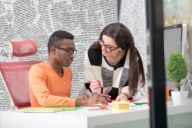Two diverse work colleagues smiling and writing down notes while sitting together at a table in a modern office royalty free stock photography