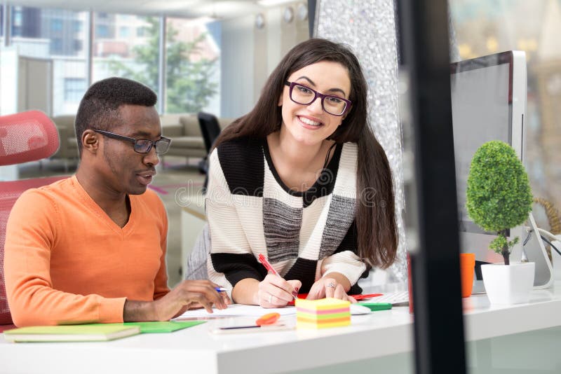 Two diverse work colleagues smiling and writing down notes while sitting together at a table in a modern office royalty free stock photography