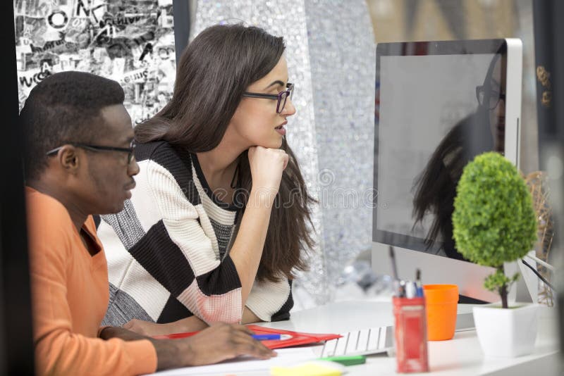 Two diverse work colleagues smiling and writing down notes while sitting together at a table in a modern office stock image