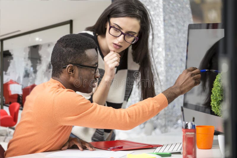 Two diverse work colleagues smiling and writing down notes while sitting together at a table in a modern office stock image