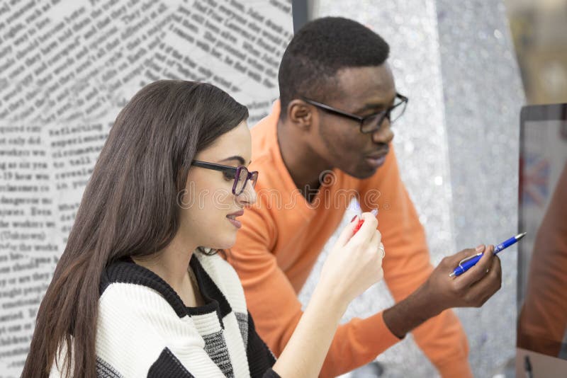 Two diverse work colleagues smiling and writing down notes while sitting together at a table in a modern office royalty free stock photo