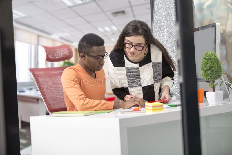 Two diverse work colleagues smiling and writing down notes while sitting together at a table in a modern office royalty free stock photography