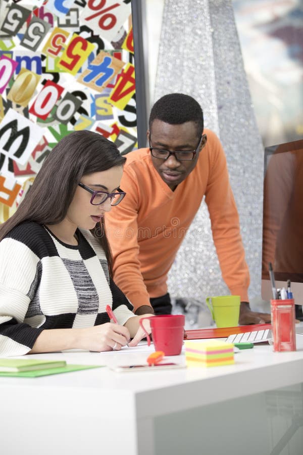 Two diverse work colleagues smiling and writing down notes while sitting together at a table in a modern office stock images
