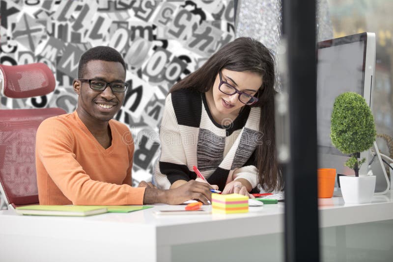 Two diverse work colleagues smiling and writing down notes while sitting together at a table in a modern office royalty free stock images