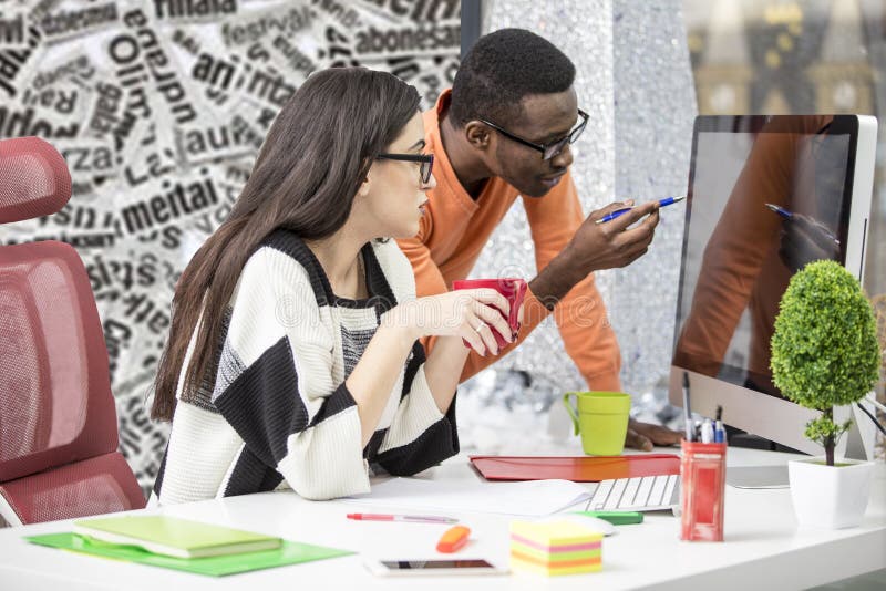 Two diverse work colleagues smiling and writing down notes while sitting together at a table in a modern office royalty free stock image