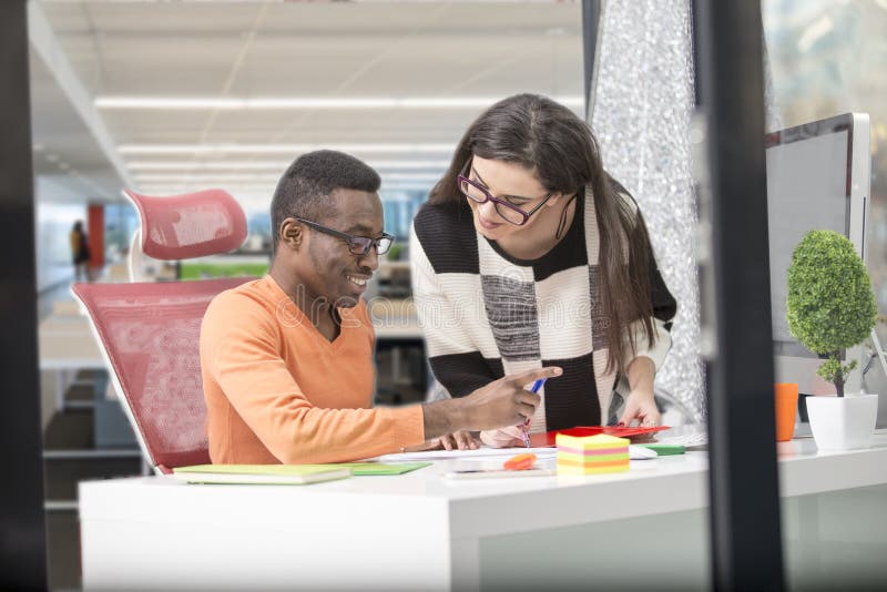 Two diverse work colleagues smiling and writing down notes while sitting together at a table in a modern office royalty free stock image