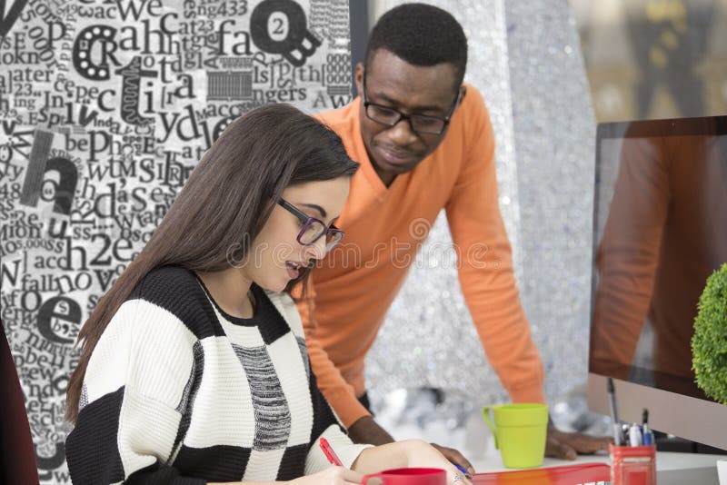 Two diverse work colleagues smiling and writing down notes while sitting together at a table in a modern office stock images