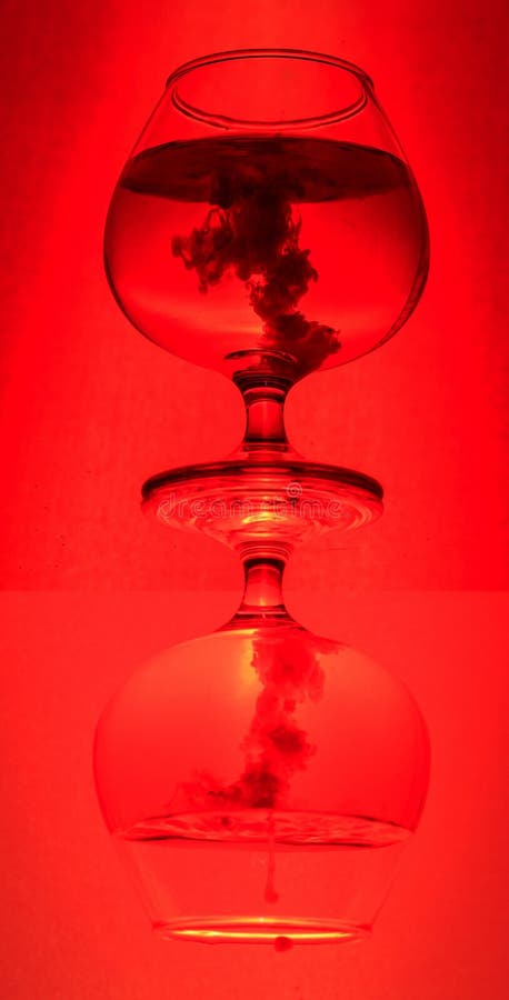 Two elegant glasses stacked and reflected, filled with a vivid red liquid, showcasing a mesmerizing swirling pattern royalty free stock images