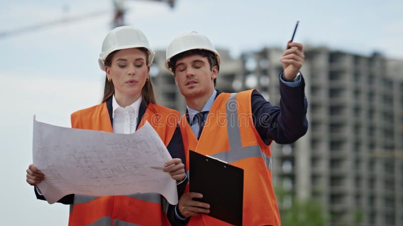 Two engineers examine blueprints discussing project at construction site closeup stock video