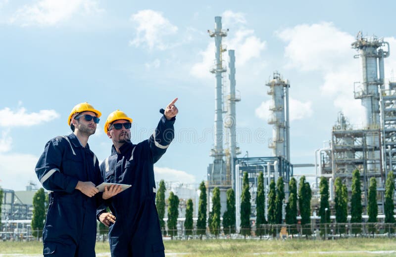 Two factory engineer or technician workers with one hold tablet and other point to right side and stand in front of refining royalty free stock photos