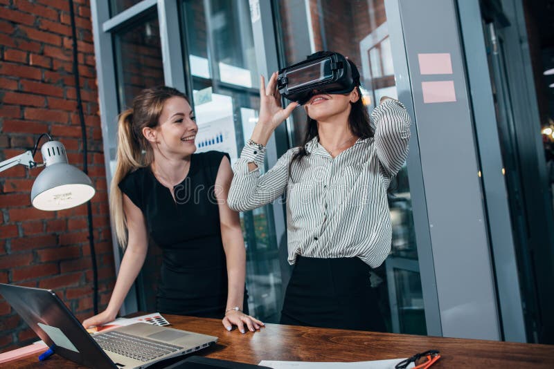 Two female application developers testing a new app designed for VR headset standing in modern office stock photography