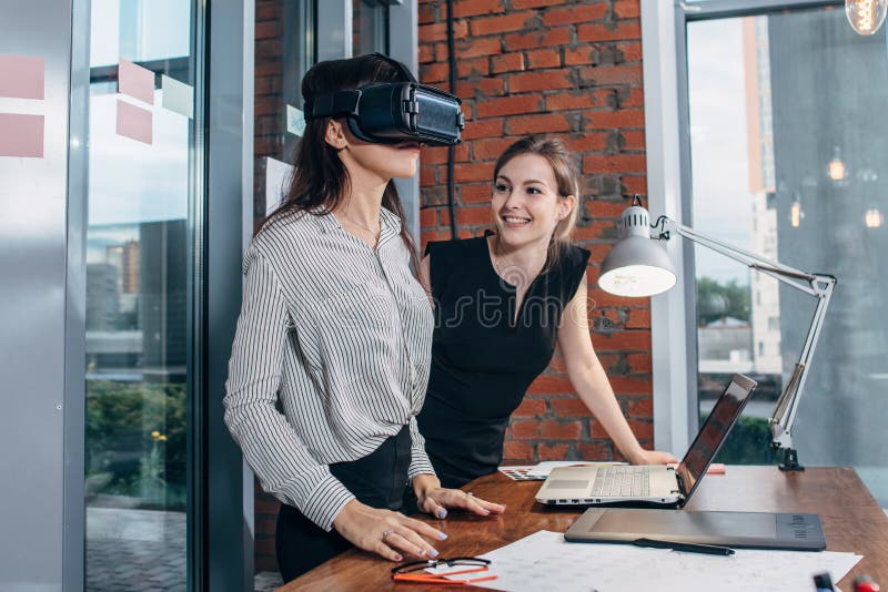 Two female application developers testing a new app designed for VR headset standing in modern office stock photos