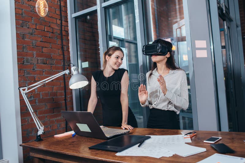 Two female application developers testing a new app designed for VR headset standing in modern office.