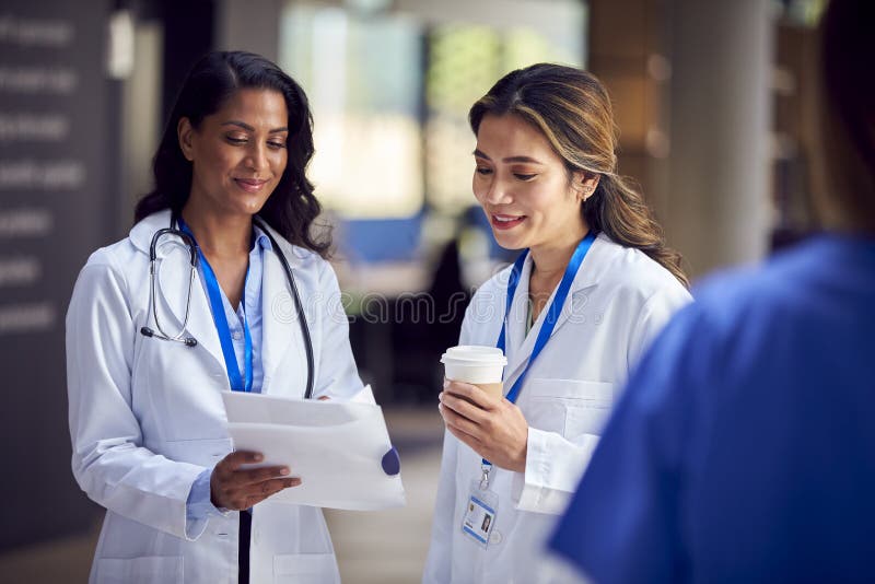 Two Female Medical Staff Wearing White Coats Discussing Patient Notes