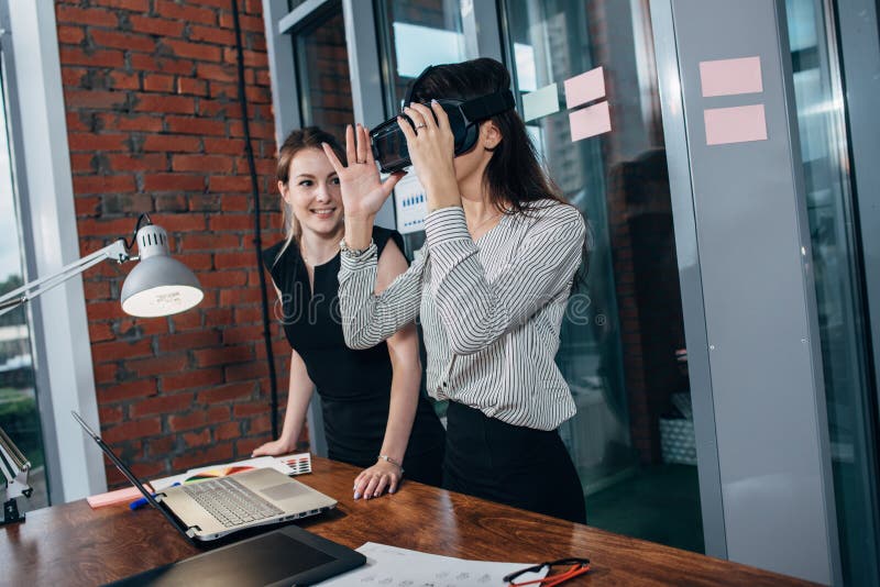 Two female students playing a 3d game in VR glasses having a break after a lesson in the classroom stock photo