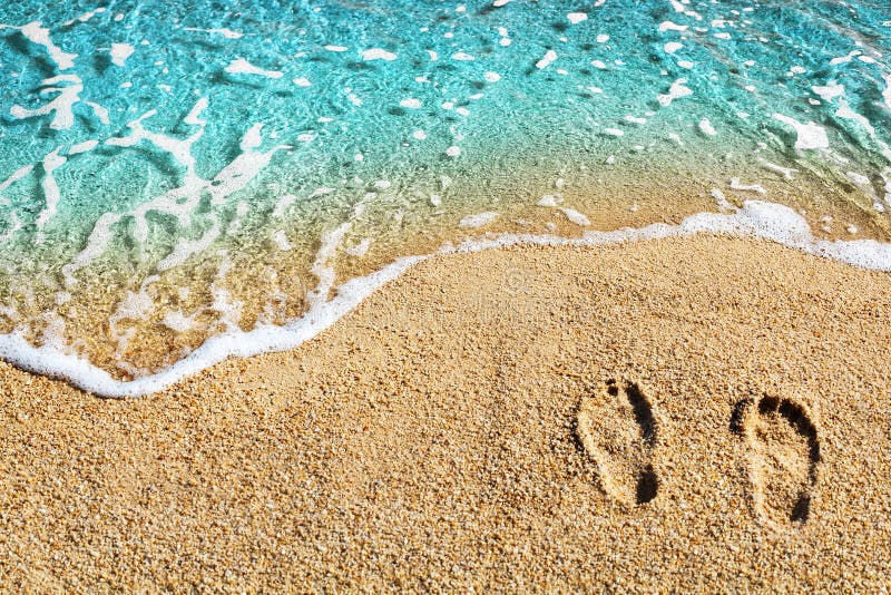 Two footprints on yellow sand, blue sea wave, white foam top view close up, turquoise ocean water, summer vacations concept