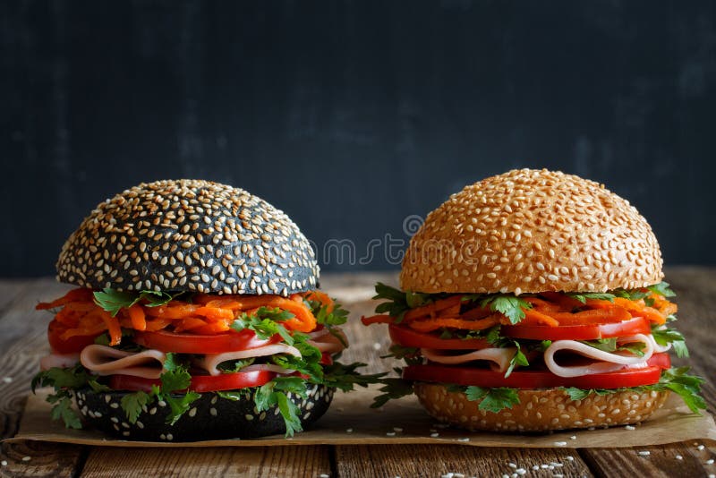 Two fresh appetizing hamburgers dark and light with sesame seeds, close-up, with fresh vegetables tomato, sweet pepper, Korean