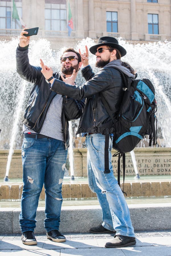 Two friends are taking a photo with a smartphone in a public place. Full figure. Making funny faces. Heavy metal signs. Two friends are taking a photo with a smartphone in a public place. Full figure. Making funny faces. Heavy metal signs.