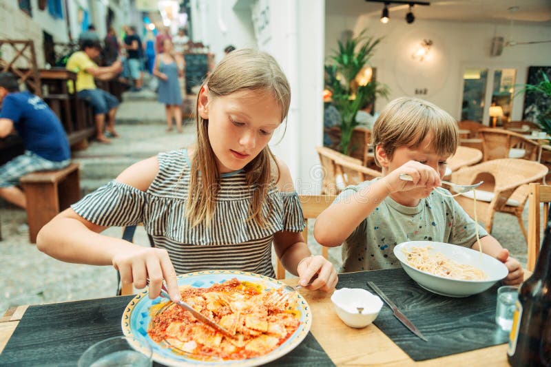 Two funny kids having lunch in the restaurant, eating ravioli and pasta