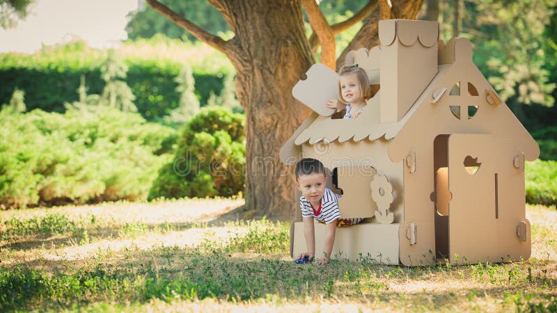 Two funny kids are playing in a cardboard toy house. In a summer day in the park