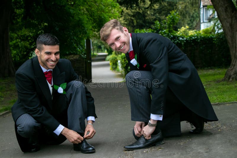 Gay couple of grooms pose for photographs whiel tying shoe laces