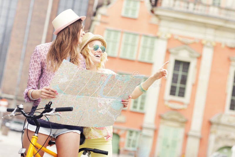 Two girl friends using map while riding tandem bicycle