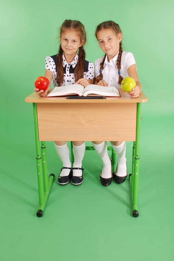 Two girl in a school uniform sitting at a desk and reading a book
