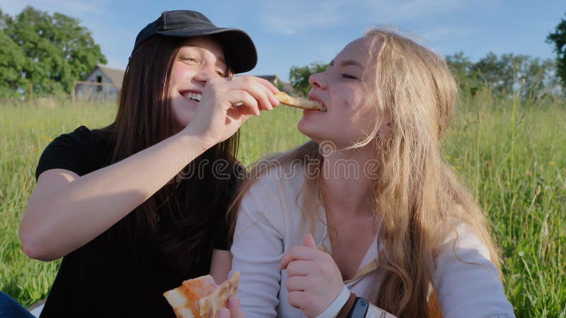 Two Girls Friends Of Schoolchildren Eat Pizza Outdoors During The Sunset In The Evening.