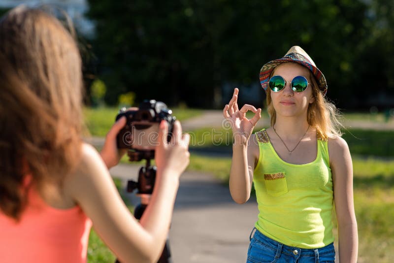 Two Girls Are Girlfriends In The Summer In City Record The Video On The Camera With A Gesture 