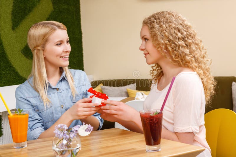 Two girls giving each other presents in cafe stock photo Two girls giving each other presents in cafe stock photo