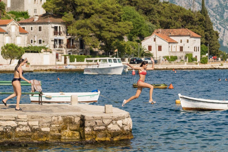 Two girls jumping from a stone pier in Perast village in Kotor bay, Montenegro